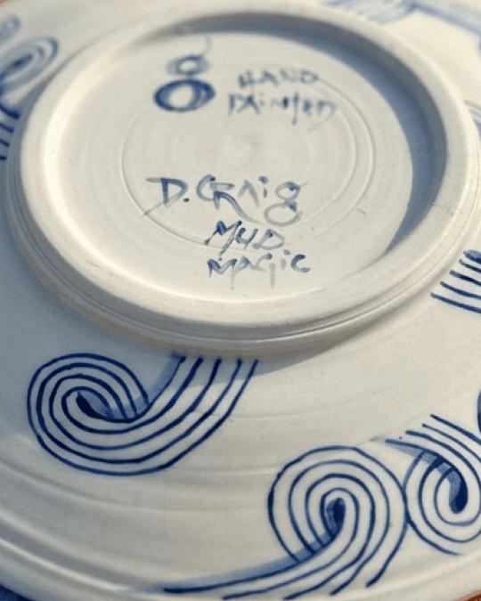 A hand-painted plate signed on the reverse, resting on a spiral-decorated dish